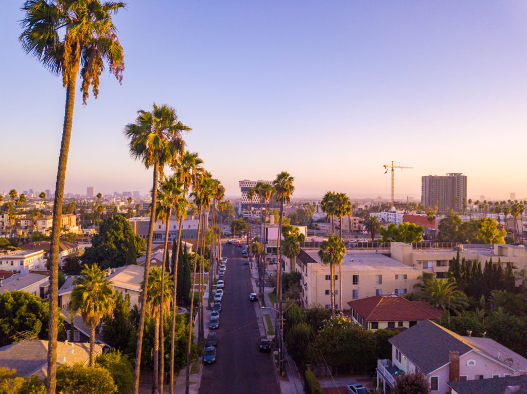 Beverly Hills street with palm trees at sunset in Los Angeles with Hollywood sign on the horizon.